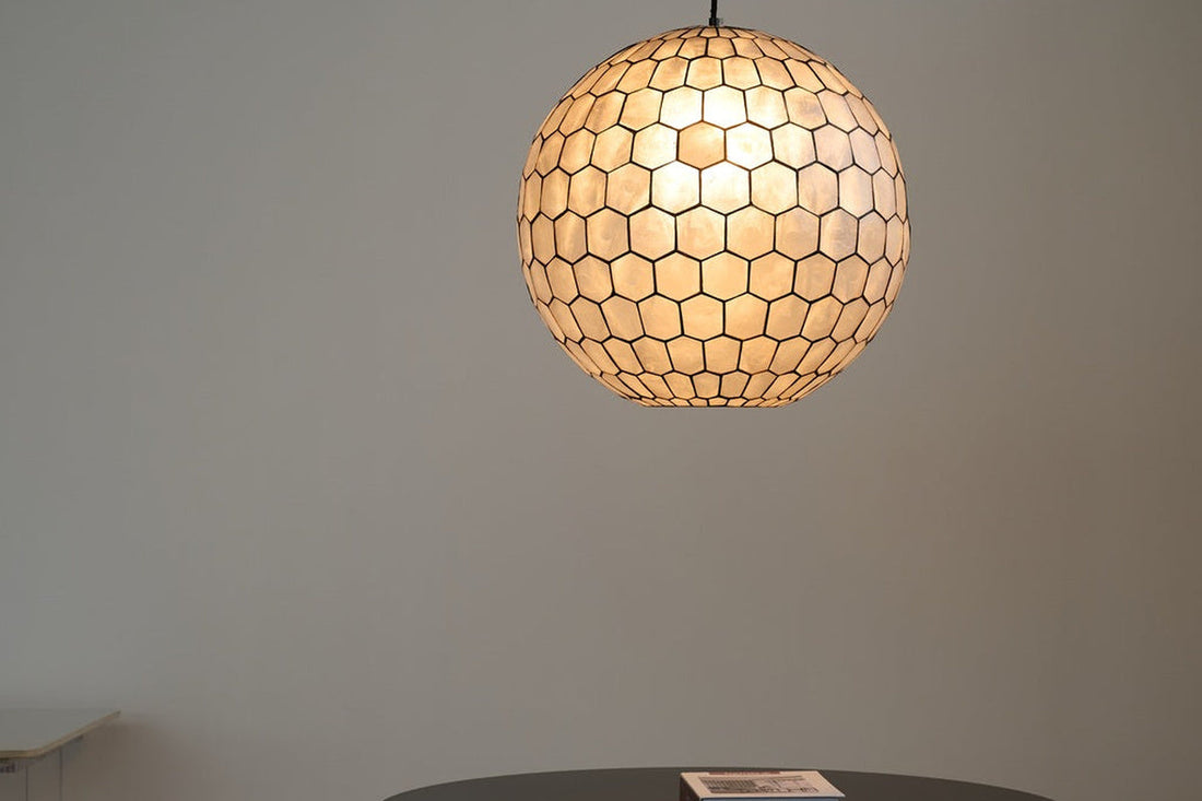 Modern Capiz Honeycomb Globe Pendant Light illuminated above a round black table, showing the spherical shell-and-grid silhouette.