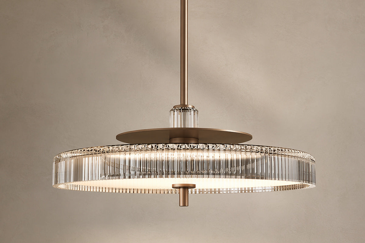 A lit crystal drum pendant with a gold-toned center against a beige wall.