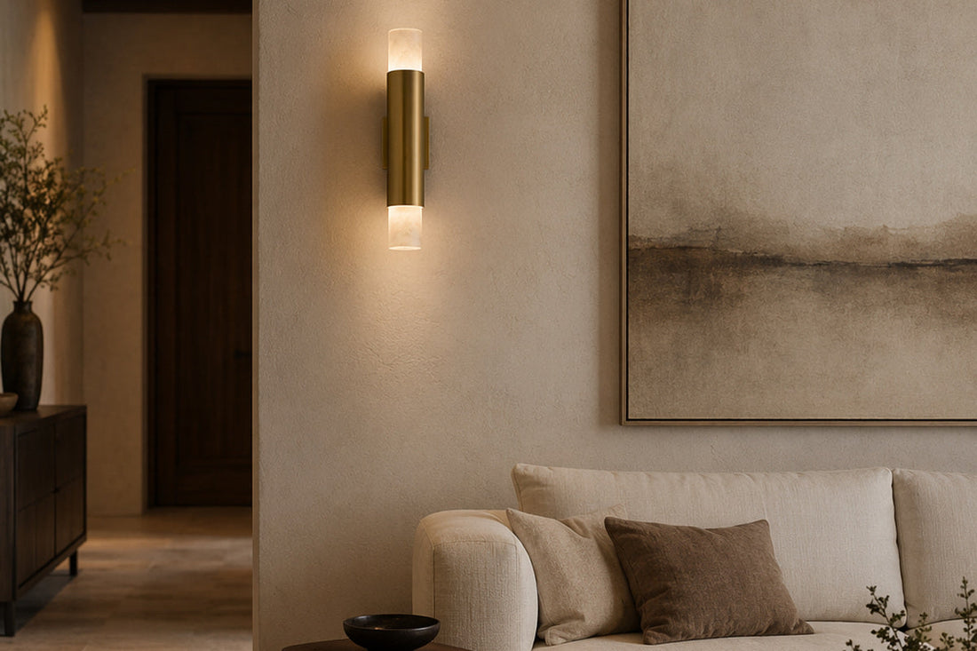 Current Shopify living-room image showing the Natural Brass and alabaster slim cylinder wall sconce illuminated beside a cream sofa.