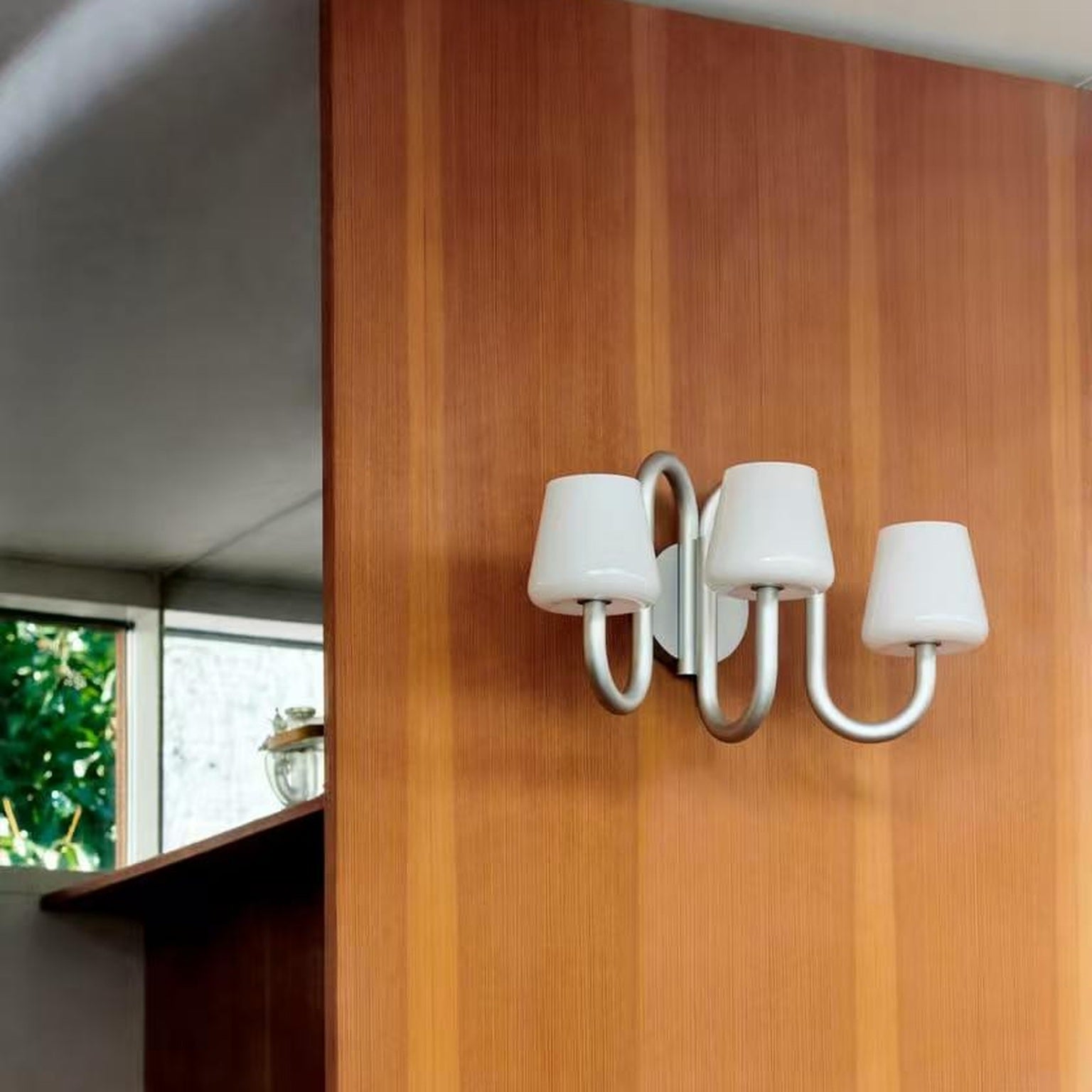 Apollo three-light wall sconce installed on a warm wood wall in the supplier photograph
