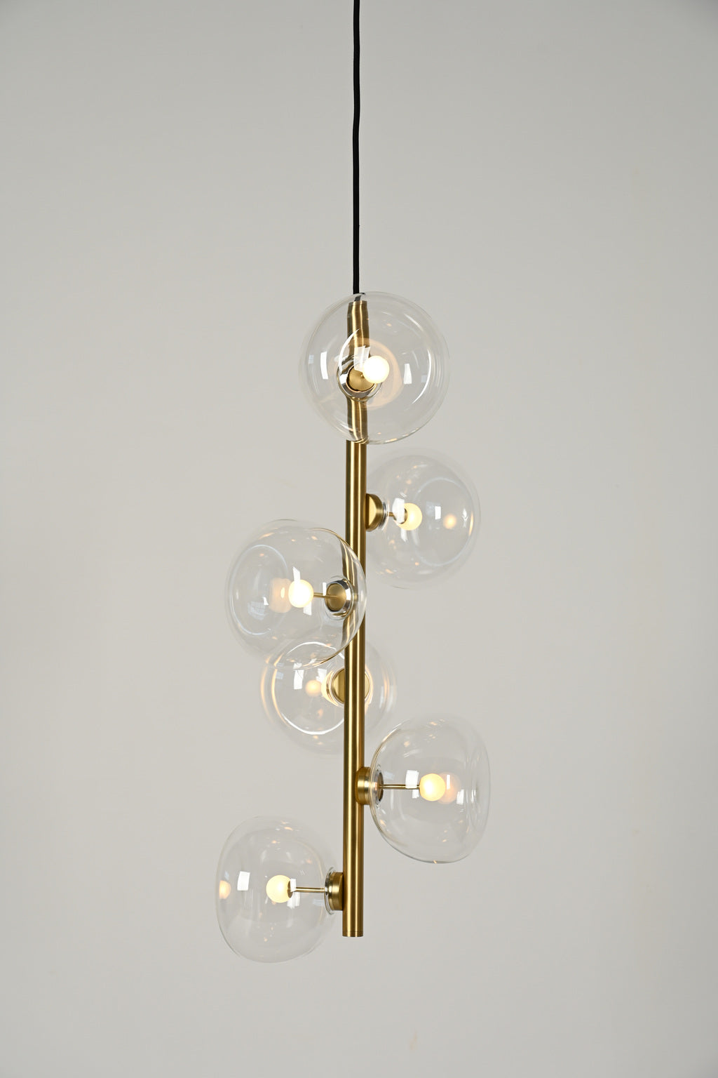 Clear glass six-light vertical pendant in Natural Brass, illuminated product view