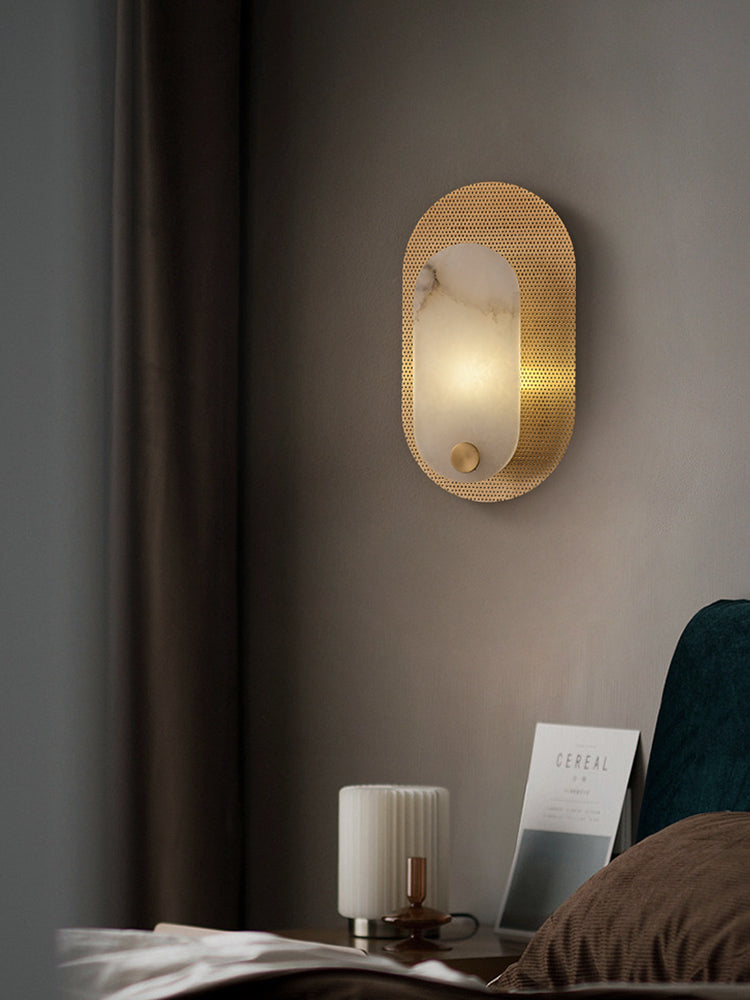 Modern Alabaster Oval Wall Sconce in Matte Gold illuminated beside a bed