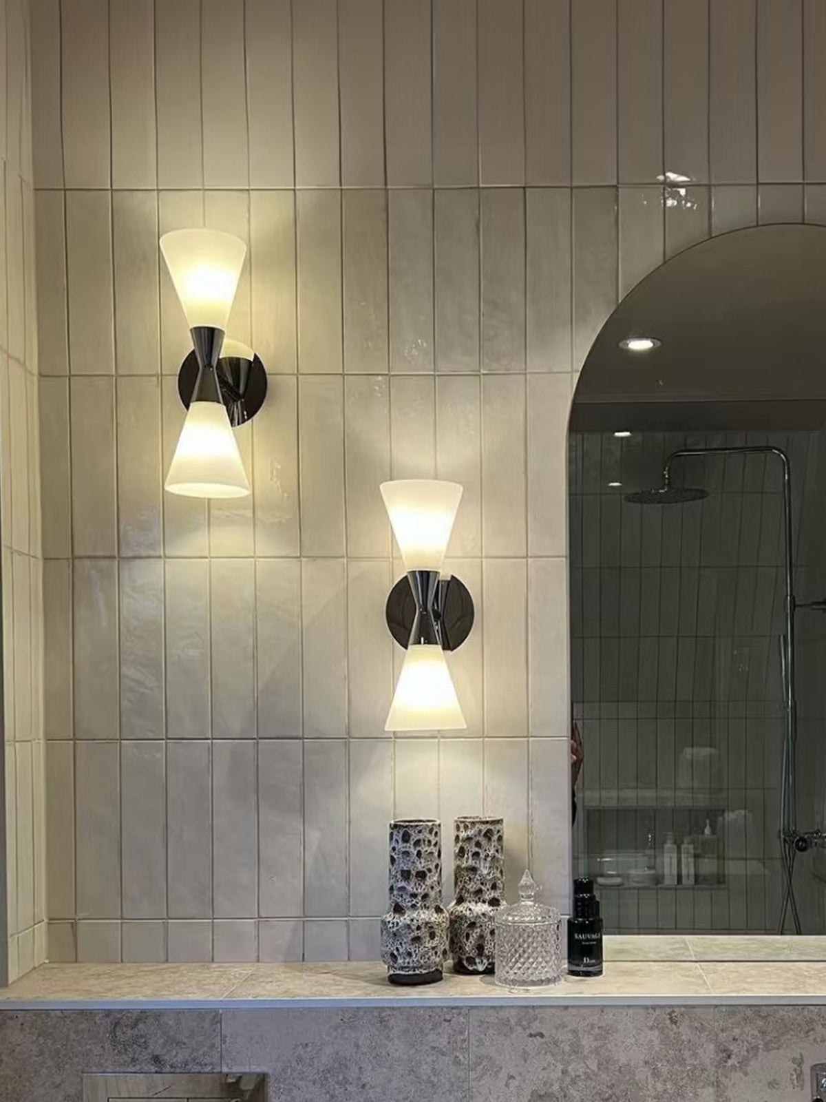 Two illuminated polished chrome double-ended frosted glass wall sconces beside a bathroom mirror