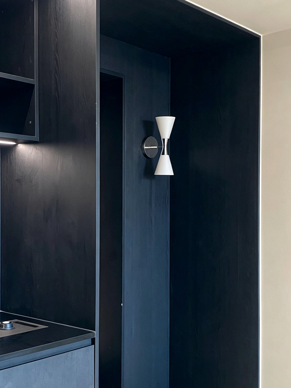Polished chrome double-ended frosted glass wall sconce on a dark blue kitchen wall