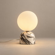 Aalia Mid-Century Marble Table Lamp on a warm greige background; Purple-veined cream marble table base; warm opal globe