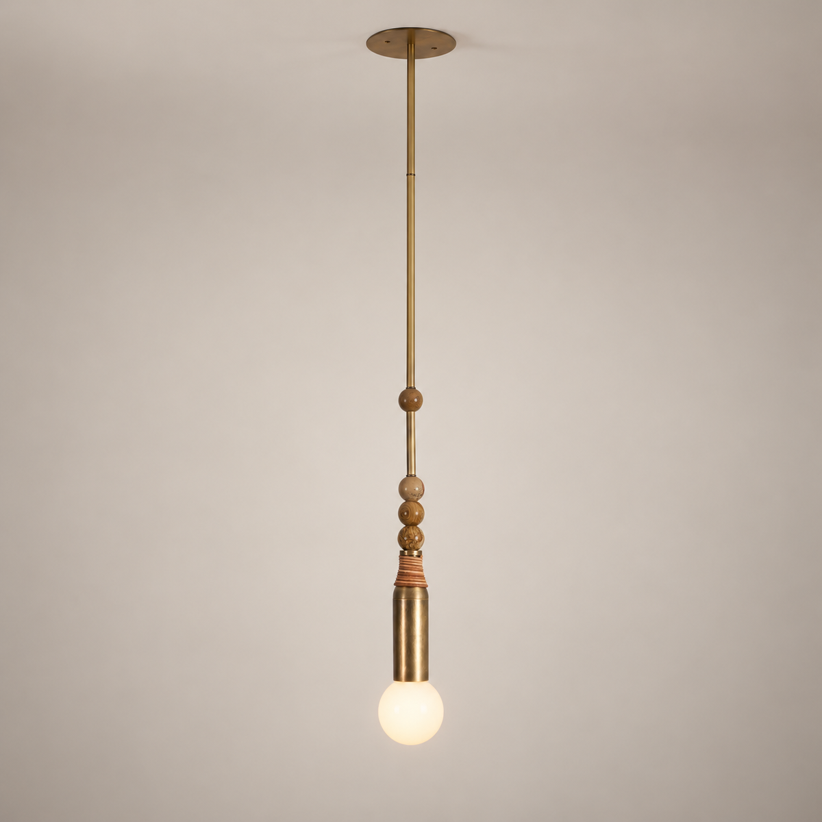 Allia Marble Pendant Light on a warm greige background; Single head; antique brass rod; four brown marble beads