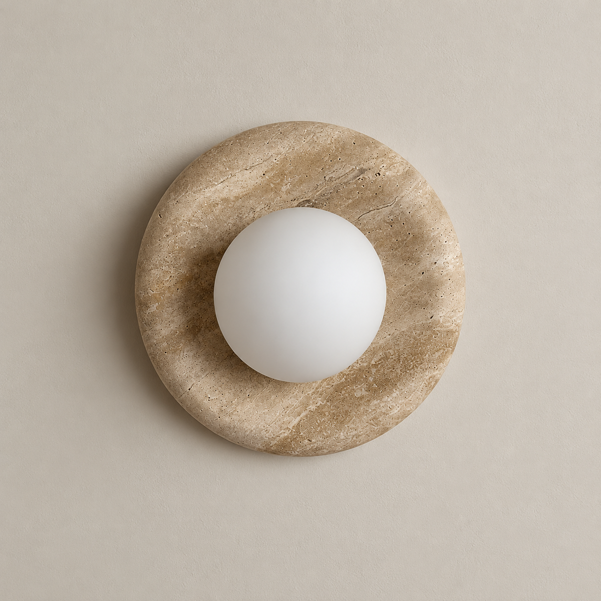 Orli Travertine Globe Wall Sconce on a warm greige background; Beige porous stone disc; globe off
