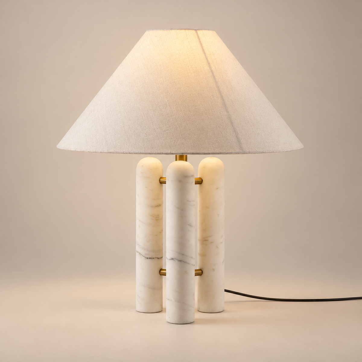 Medici Marble Table Lamp with Fabric Shade on a warm greige background; White fabric shade; three white Carrara marble pillars and brass supports