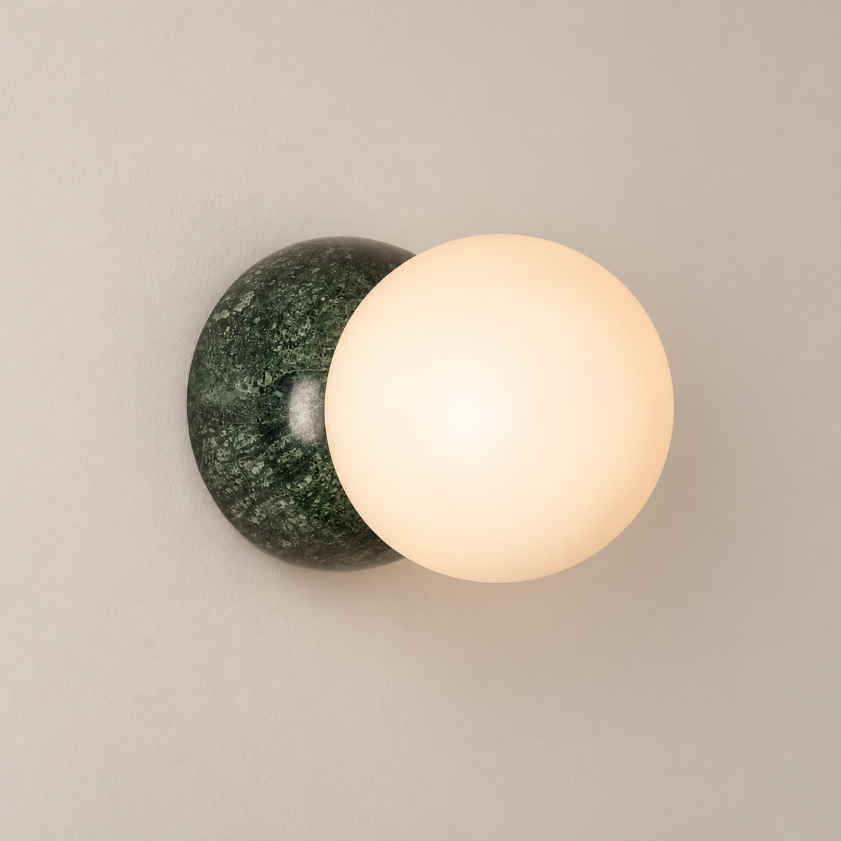 Eclipse Disc Marble Wall Sconce on a warm greige background; Green hemispherical marble wall back with white opal globe