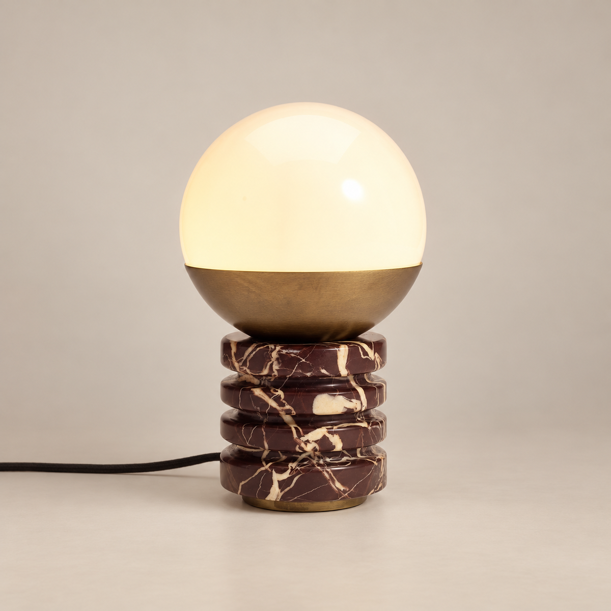 Sylvia Marble Table Lamp with Brass and Glass Shade on a warm greige background; Purple red marble four rounded ribs; brass bowl and opal globe