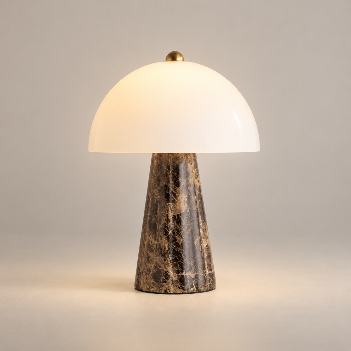 Carme Marble LED Table Lamp on a warm greige background; Carme brownmarble taperedbase whiteopal hemisphere brassfinial