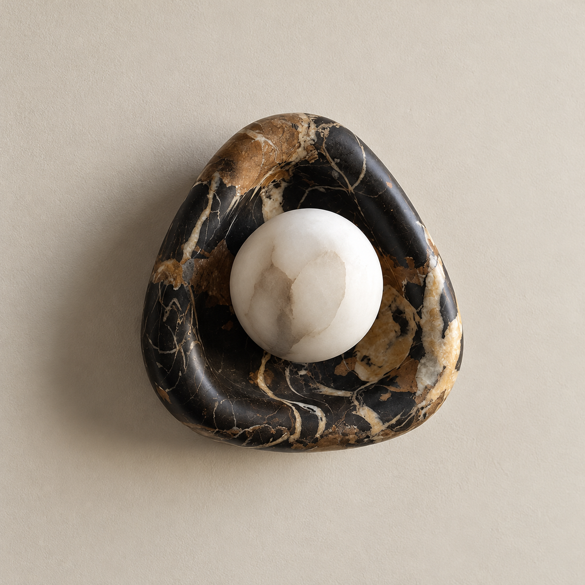 Black Organic Modern Pearl Marble Wall Sconce on a warm greige background; Black amber marble pebble bowl and white alabaster globe off