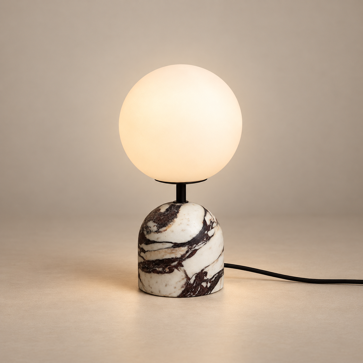Yannick Marble Globe Table Lamp on a warm greige background; Small white marble base with black socket and glass globe