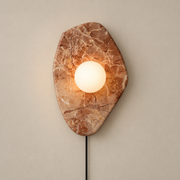 Organic Modern Textured Marble Plug-In Wall Sconce on a warm greige background; Pink organic marble plate and white glass globe, plug in cord