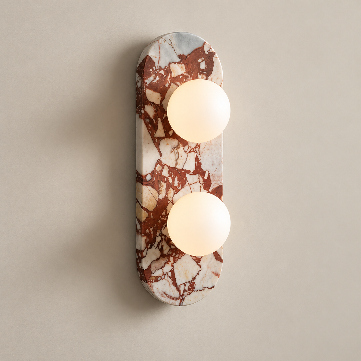 Gramercy Marble Globe Wall Sconce on a warm greige background; Red breccia marble capsule wall sconce with two white glass globes