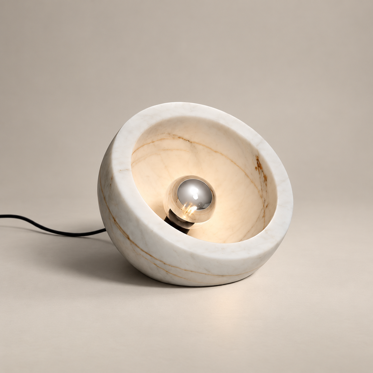 Tsuki Organic Modern Marble Table Lamp on a warm greige background; White marble tilted bowl, silver mirrored bulb