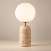 Aseneth Travertine Globe Table Lamp on a warm greige background; Model A straight brass neck