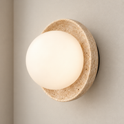 Beige travertine wall sconce with projecting opal glass globe mounted on a warm greige wall