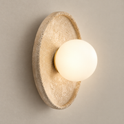 Riley Japandi Travertine Wall Sconce on a warm greige background; Riley beige stone round dish / white globe