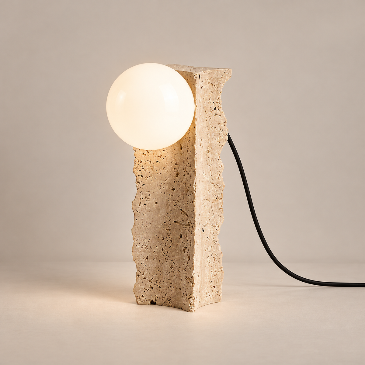 Conduit Wabi-Sabi Travertine Table Lamp on a warm greige background; Conduit rough cruciform beige stone / upper side white globe