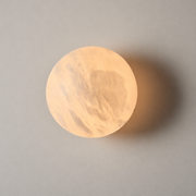 Alabaster globe wall sconce with a warm illuminated natural stone shade on a neutral greige wall