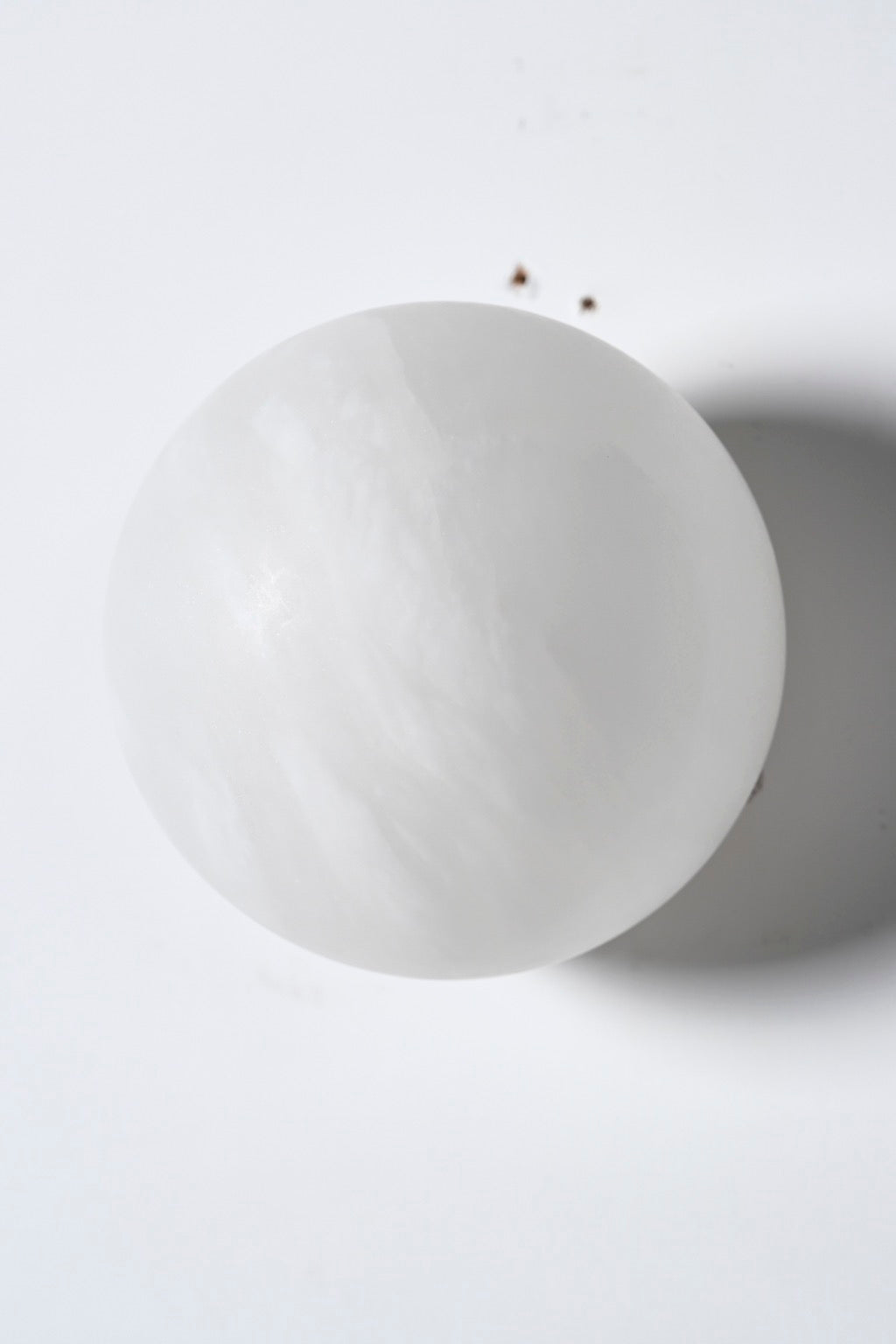 Alabaster globe wall sconce switched off, showing the curved natural stone shade