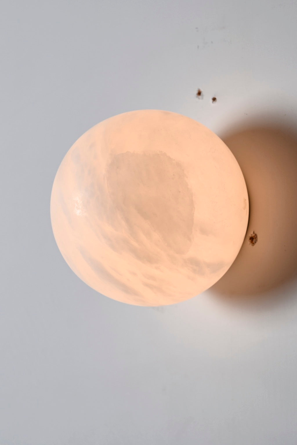 Original product photograph of the illuminated alabaster globe wall sconce from a slight side angle