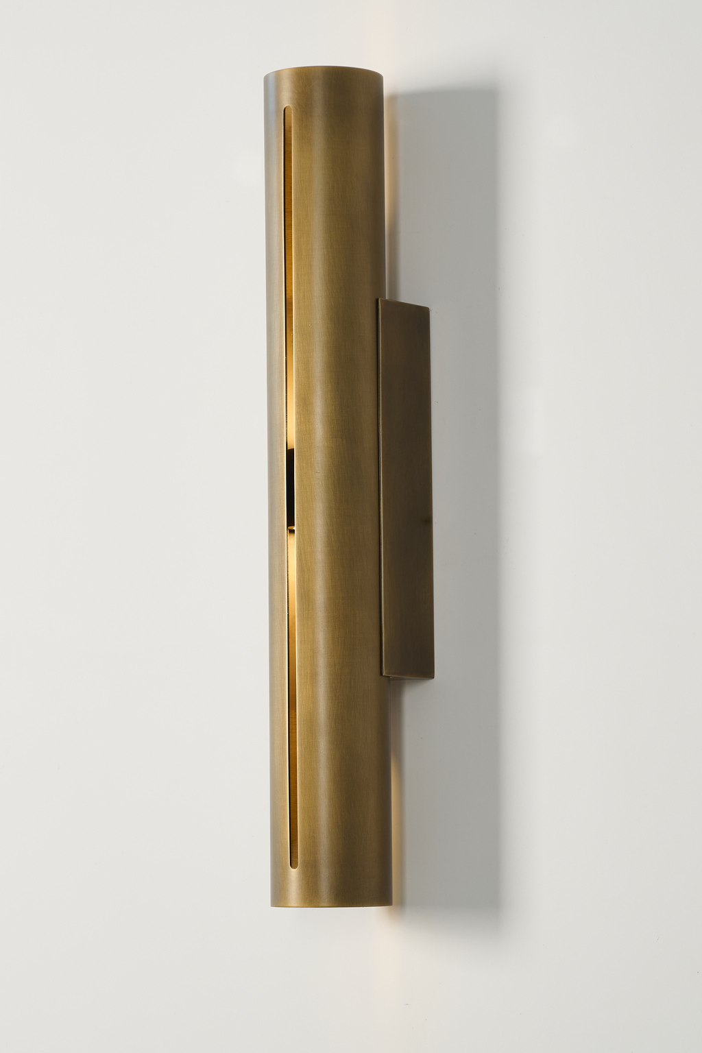 Long antique brass cylinder wall sconce, illuminated side view with mounting plate