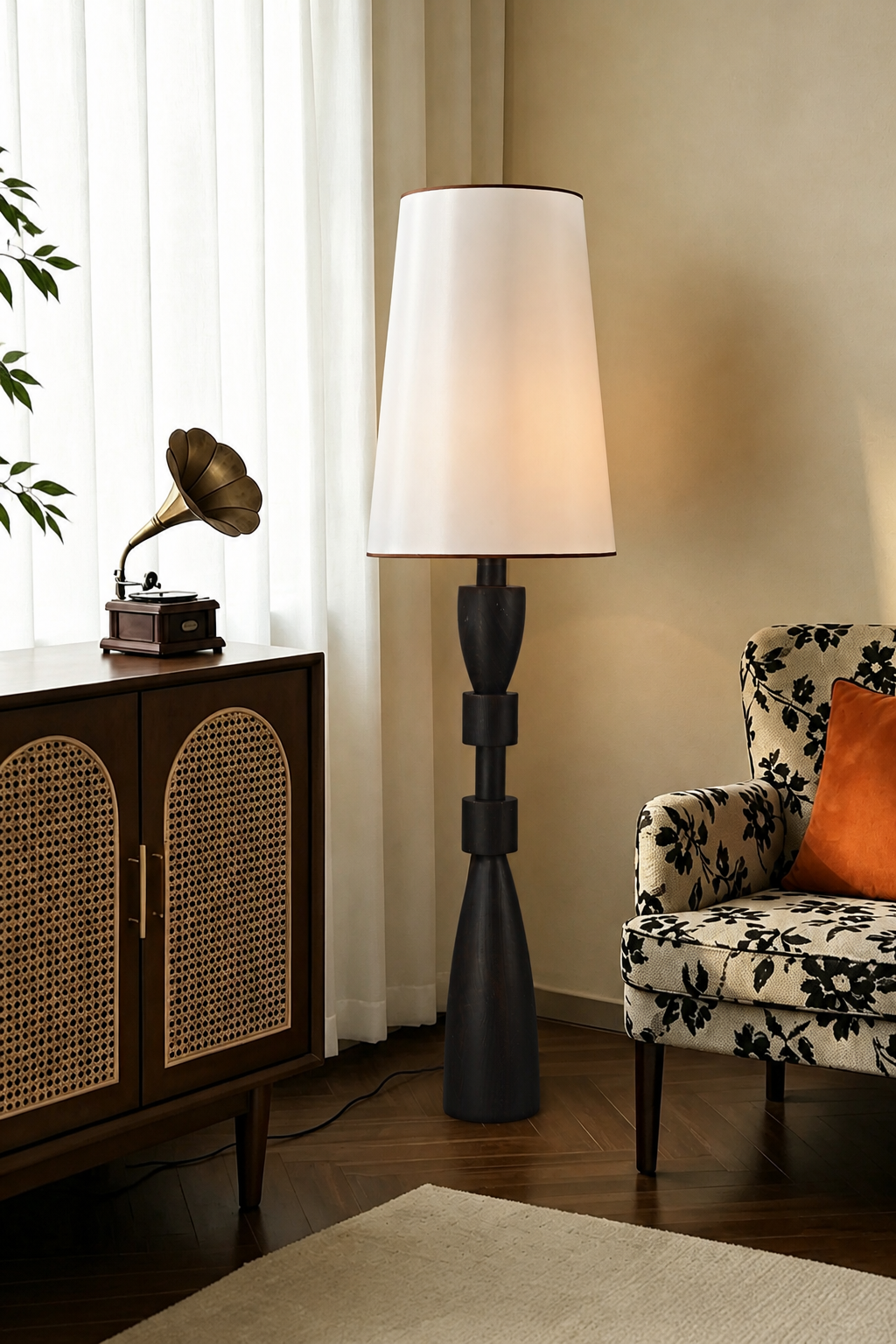 White-shaded camphor wood floor lamp near a rattan cabinet and floral chair
