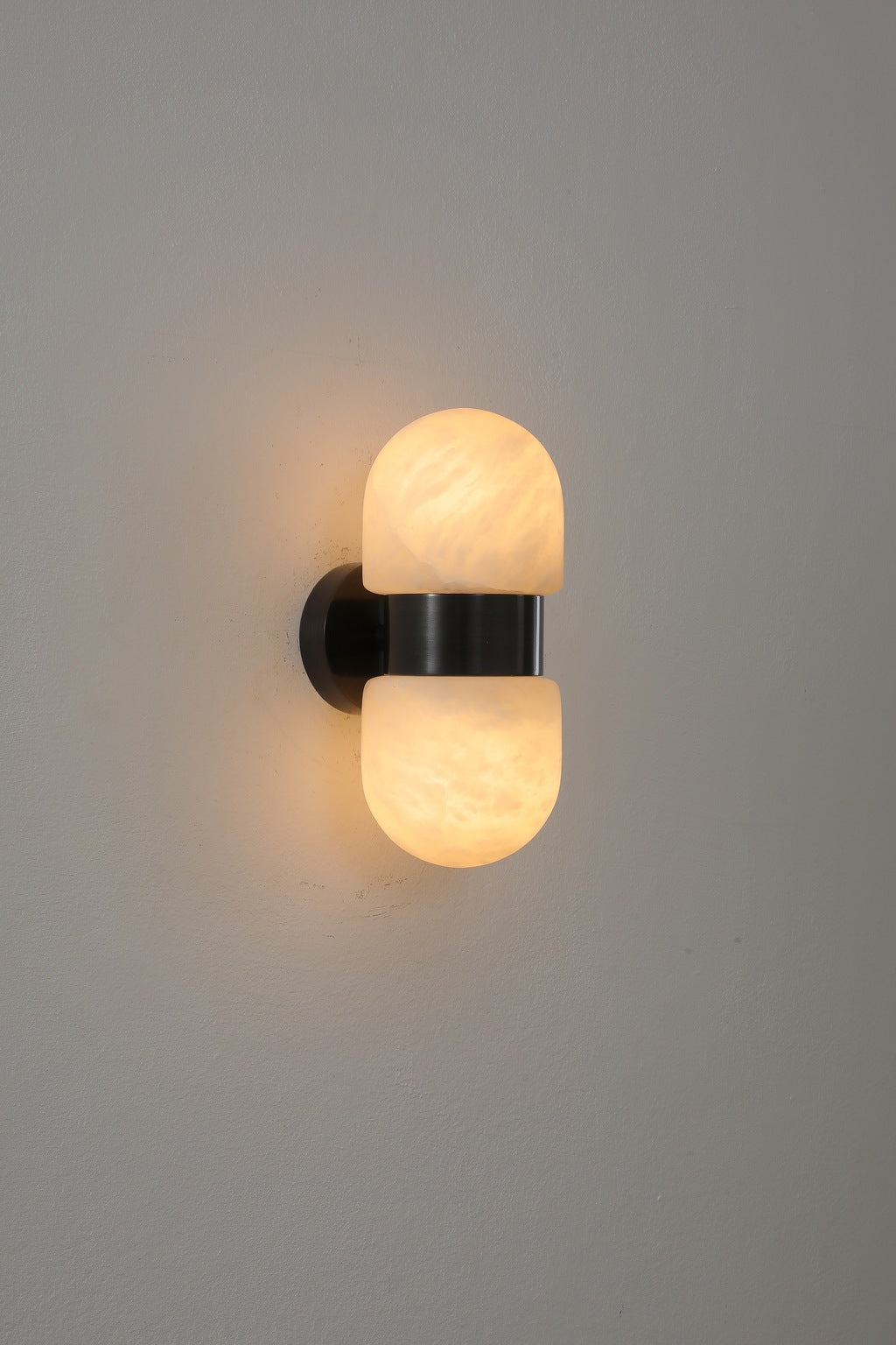 Alabaster Double Capsule Wall Sconce — Black with gold accents finish illuminated, original product photograph