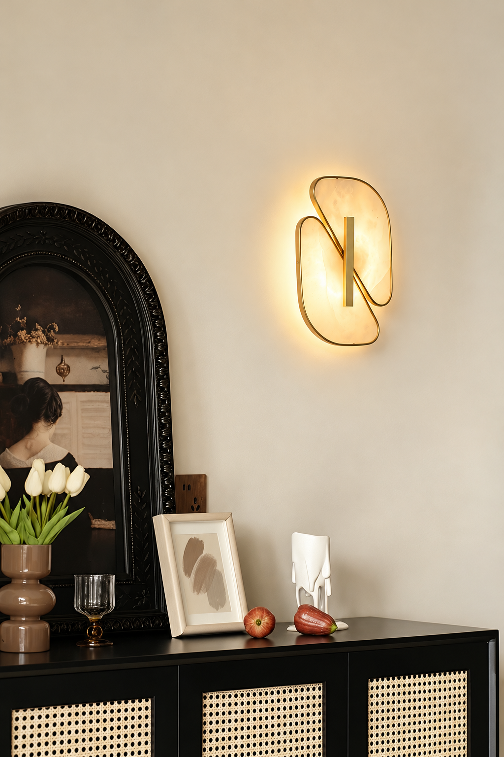 Illuminated alabaster sconce above a black console beside an ornate mirror