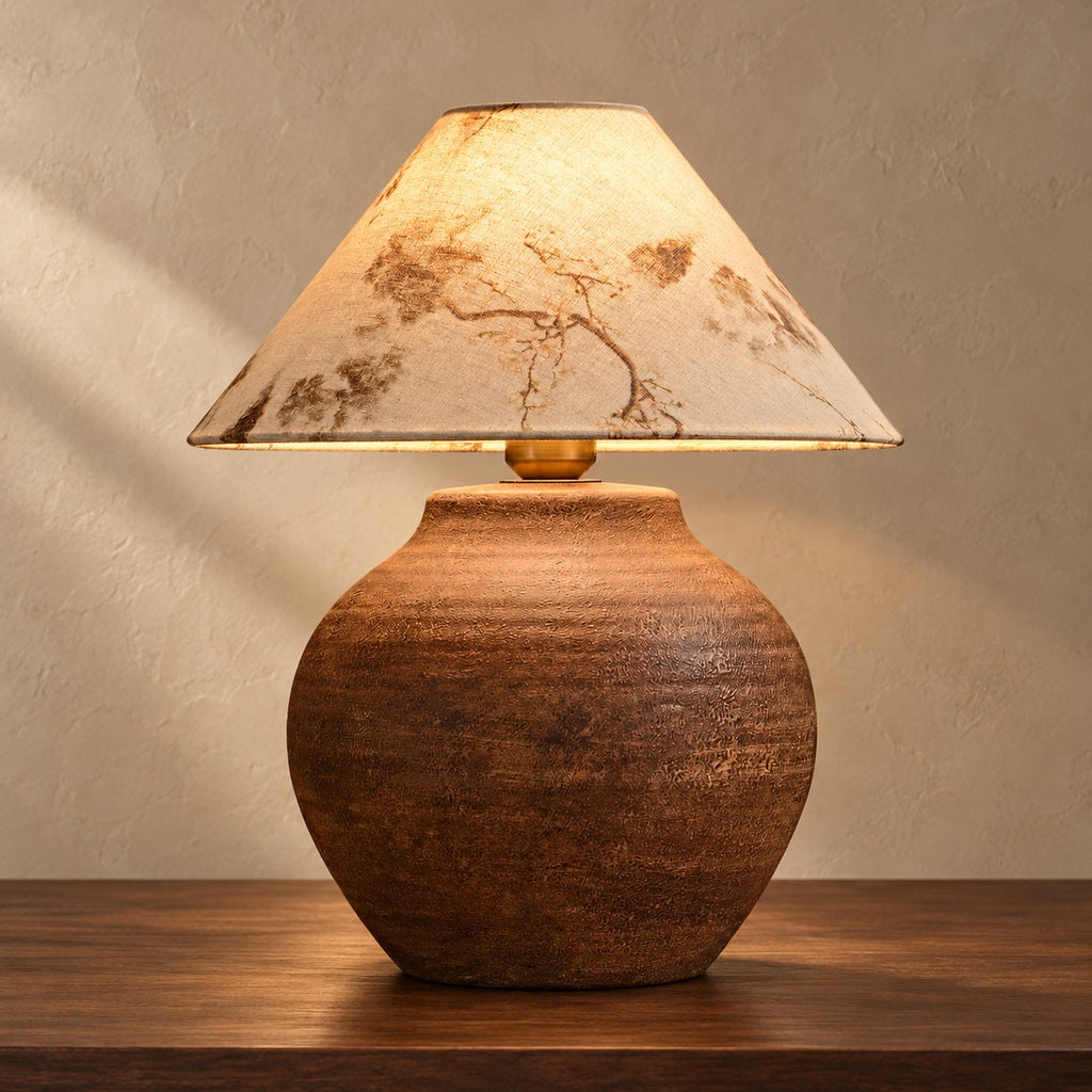 Cairnelle aged brown ceramic table lamp illuminated on a warm taupe surface