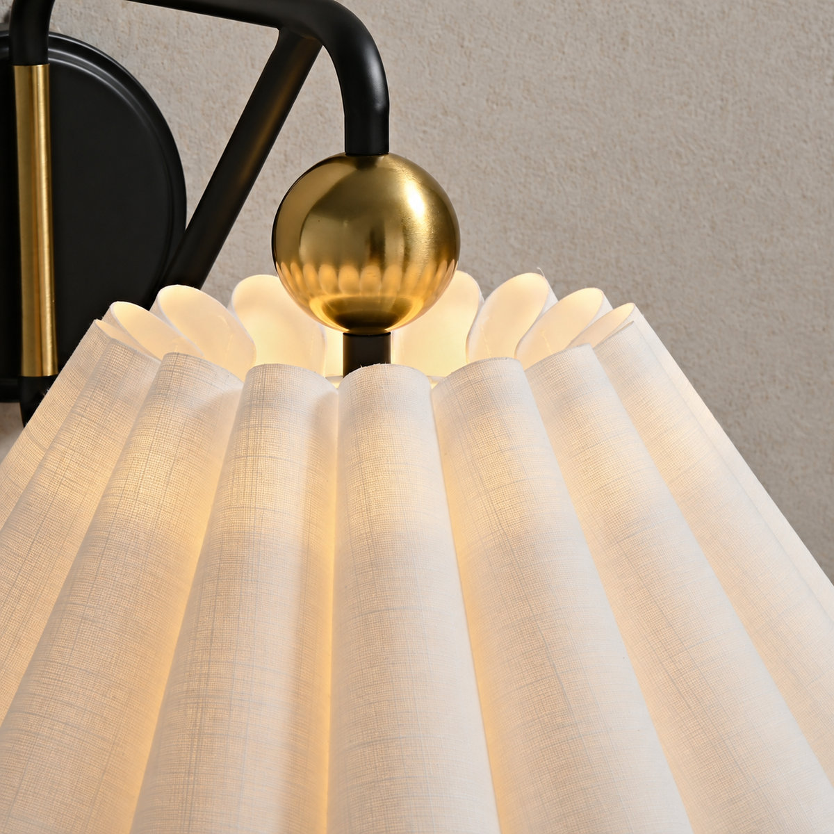 Pleated woven fabric shade and brass-tone sphere detail on the illuminated wall sconce