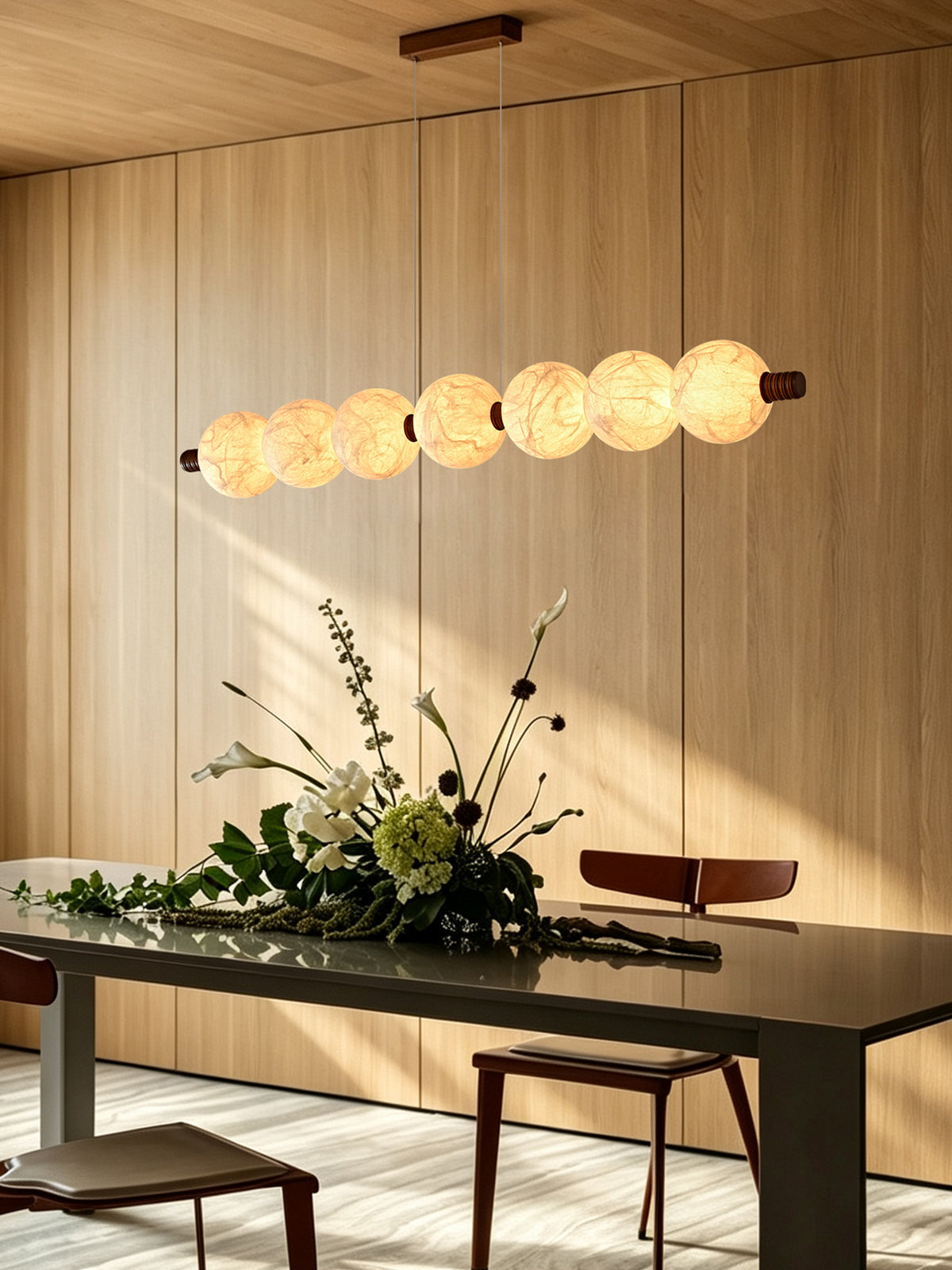 Seven-globe natural mulberry silk linear pendant with wood details, lit above a dining table in an angled room view