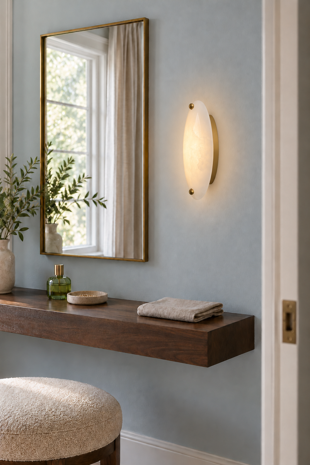White stone wall sconce glowing beside a dressing mirror