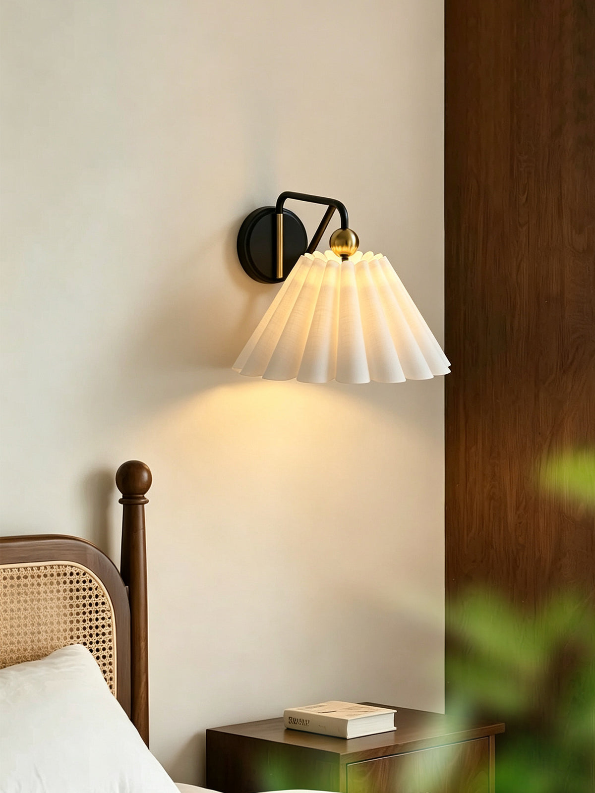 Pleated fabric wall sconce illuminated beside a bed