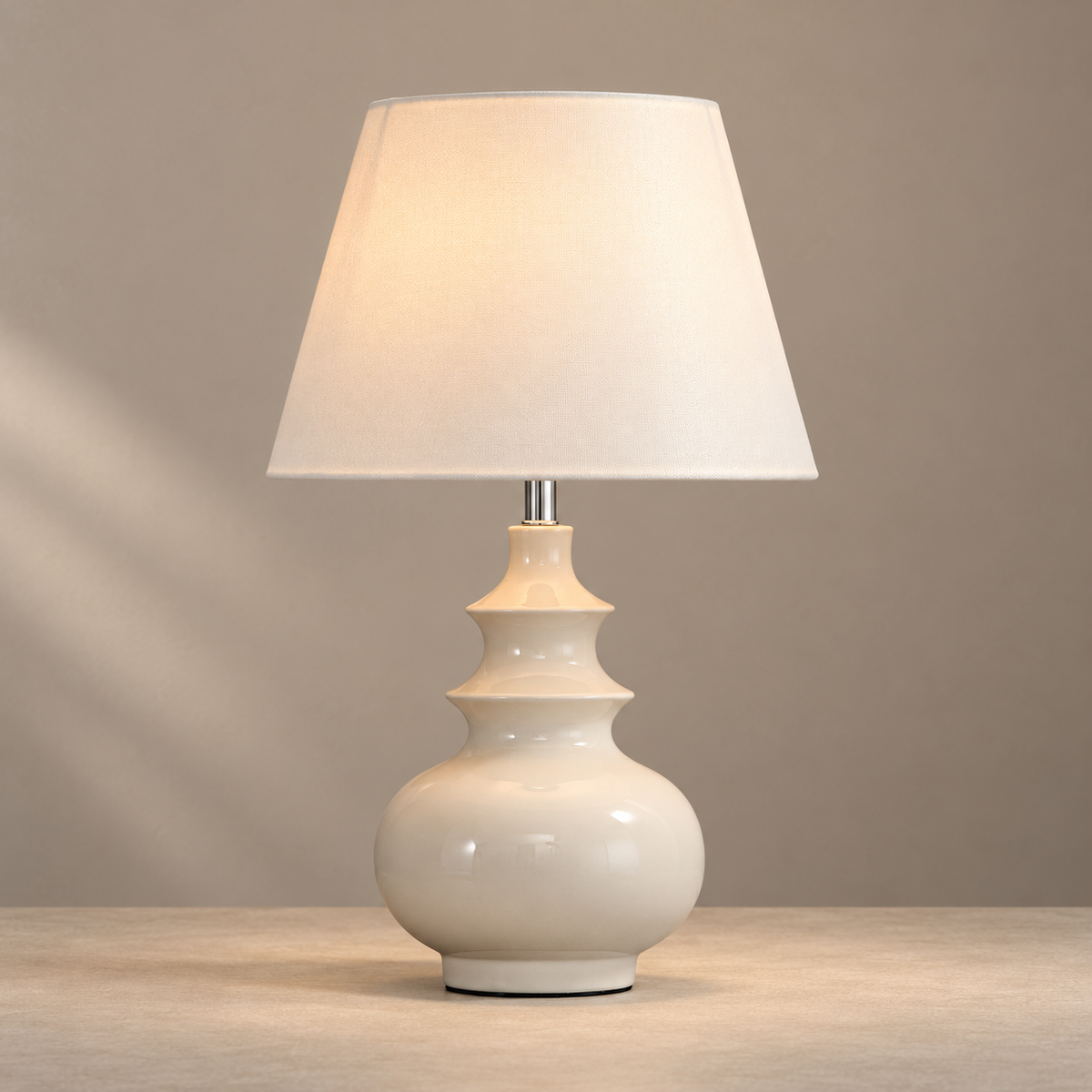 Ivory sculptural ceramic table lamp with a plain fabric shade illuminated on a warm neutral console