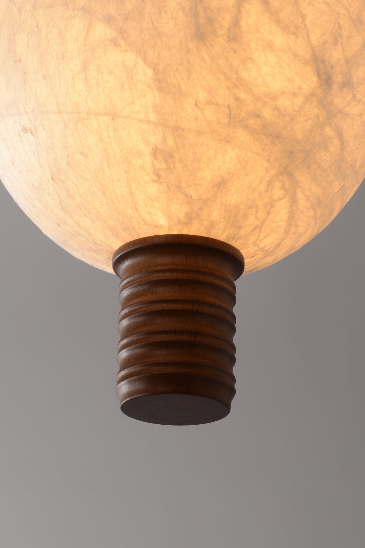 Real close-up of natural mulberry silk shade glowing above the dark wood lower endcap