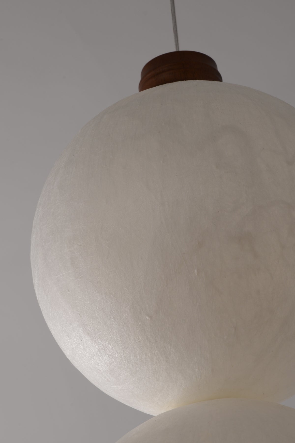 Real close-up of unlit natural mulberry silk shade, dark wood upper collar and suspension cable