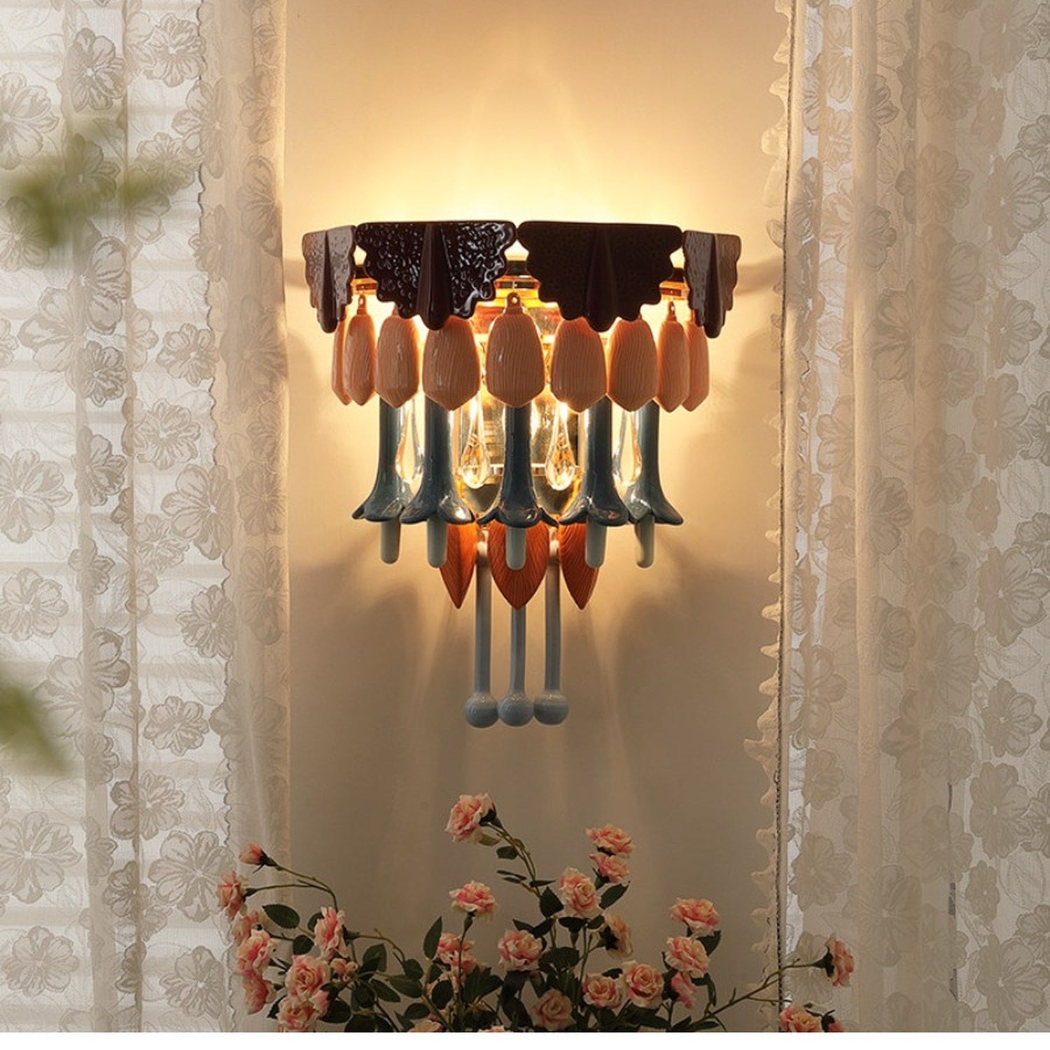 Colorful ceramic and glass wall sconce glowing between soft curtains